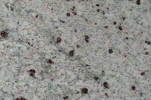 A light cream granite with soft gray movement and scattered burgundy speckling.