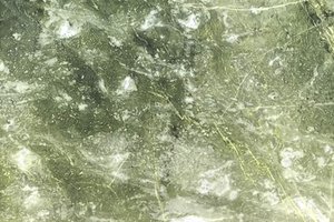 A green marble with olive tones, soft white movement, and thin gold veining.